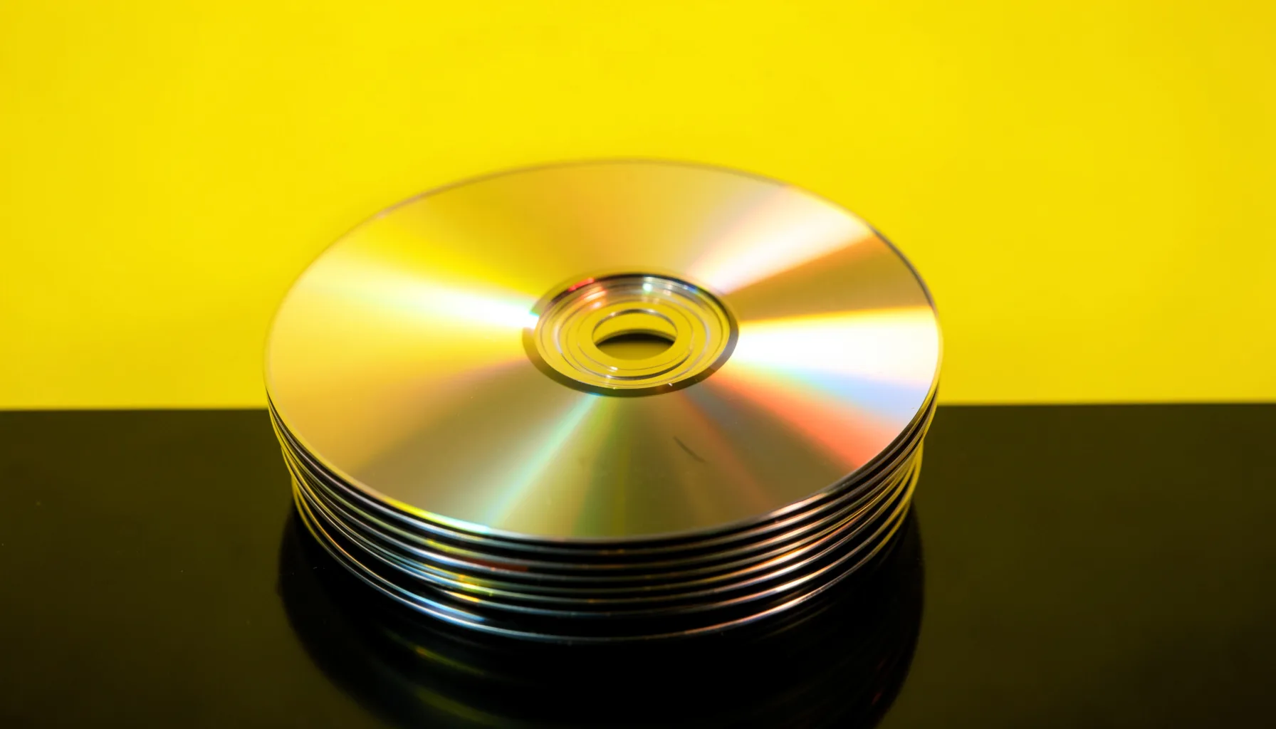 Стопка DVD-дисков с золотистыми бликами на чёрном глянцевом фоне
